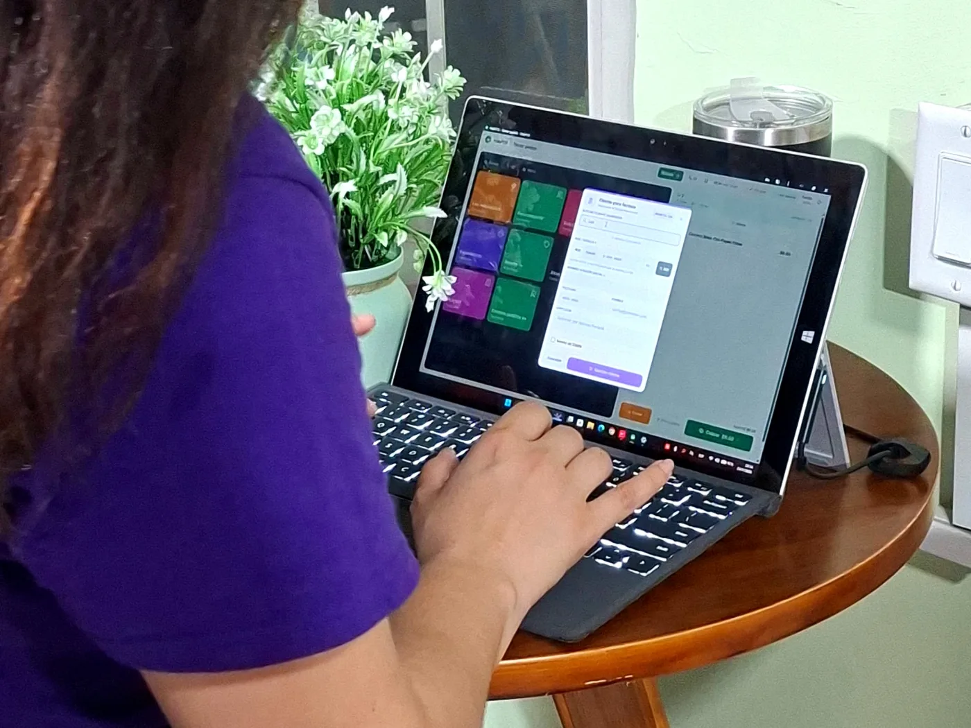 Una mujer de camisa morada escribe en el teclado de una laptop apoyada en un atril, con un cuadro emergente de pedido abierto en la pantalla.
