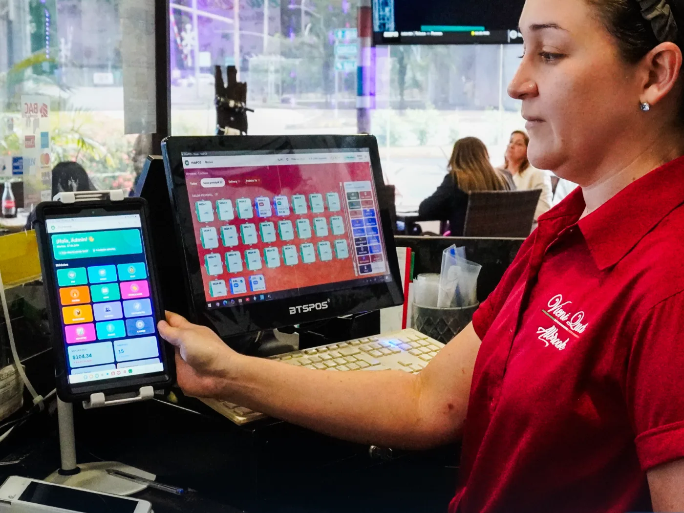 Colaboradora de Vieni Quá Albrook con una tablet que muestra el tablero de HubPOS, junto al monitor con el plano del salón